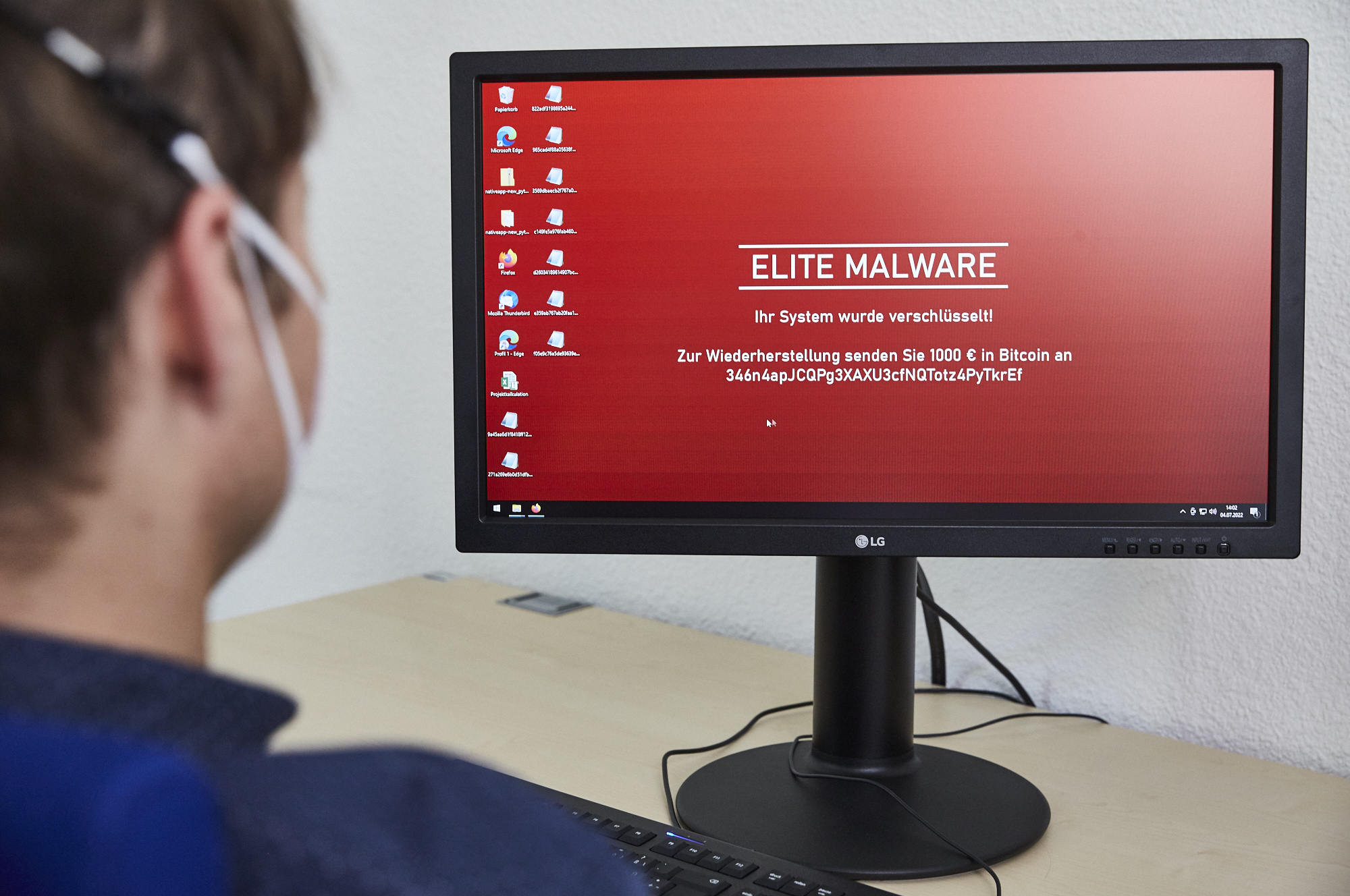 A man looks at a computer screen that shows a red desktop background with an extortion message.