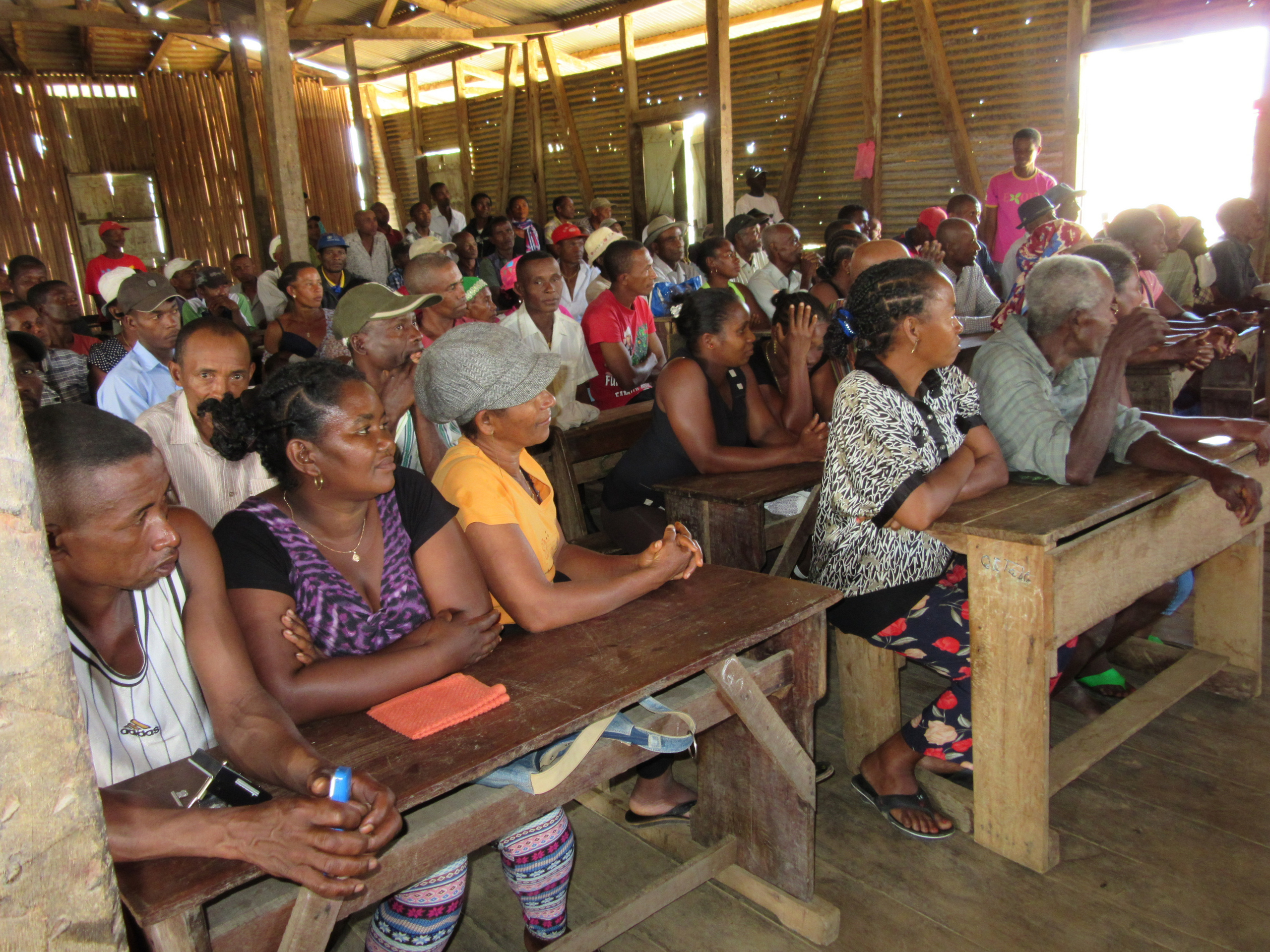 [Translate to Englisch:] Vanillebauern und Vanillebäuerinnen auf Madagaskar sitzen bei einer Veranstaltung auf Schulbänken. 