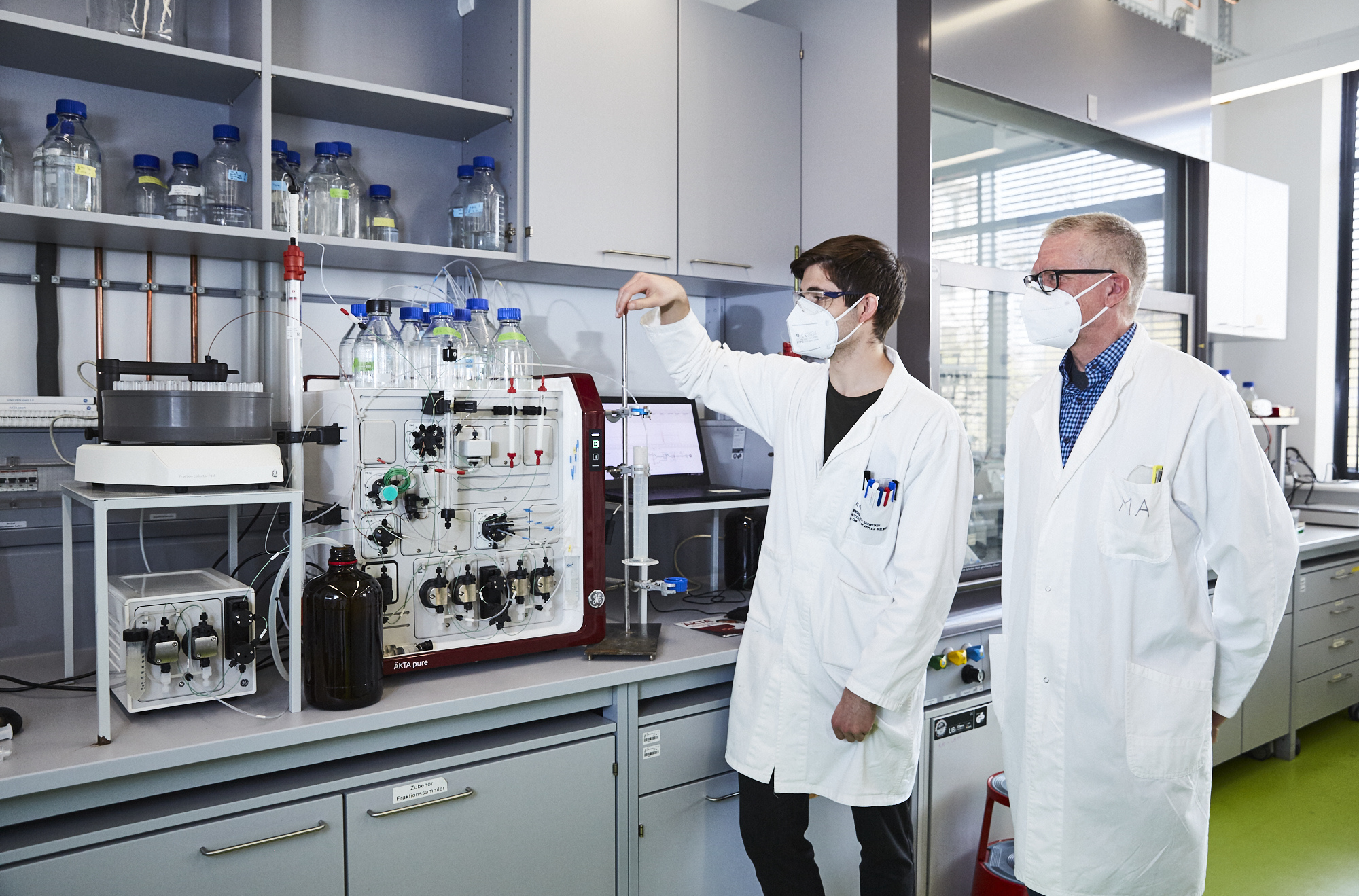 [Translate to Englisch:] Prof. Meyer-Almes und ein Student stehen im Labor vor einem Abzug mit einer Destillationsanlage. 