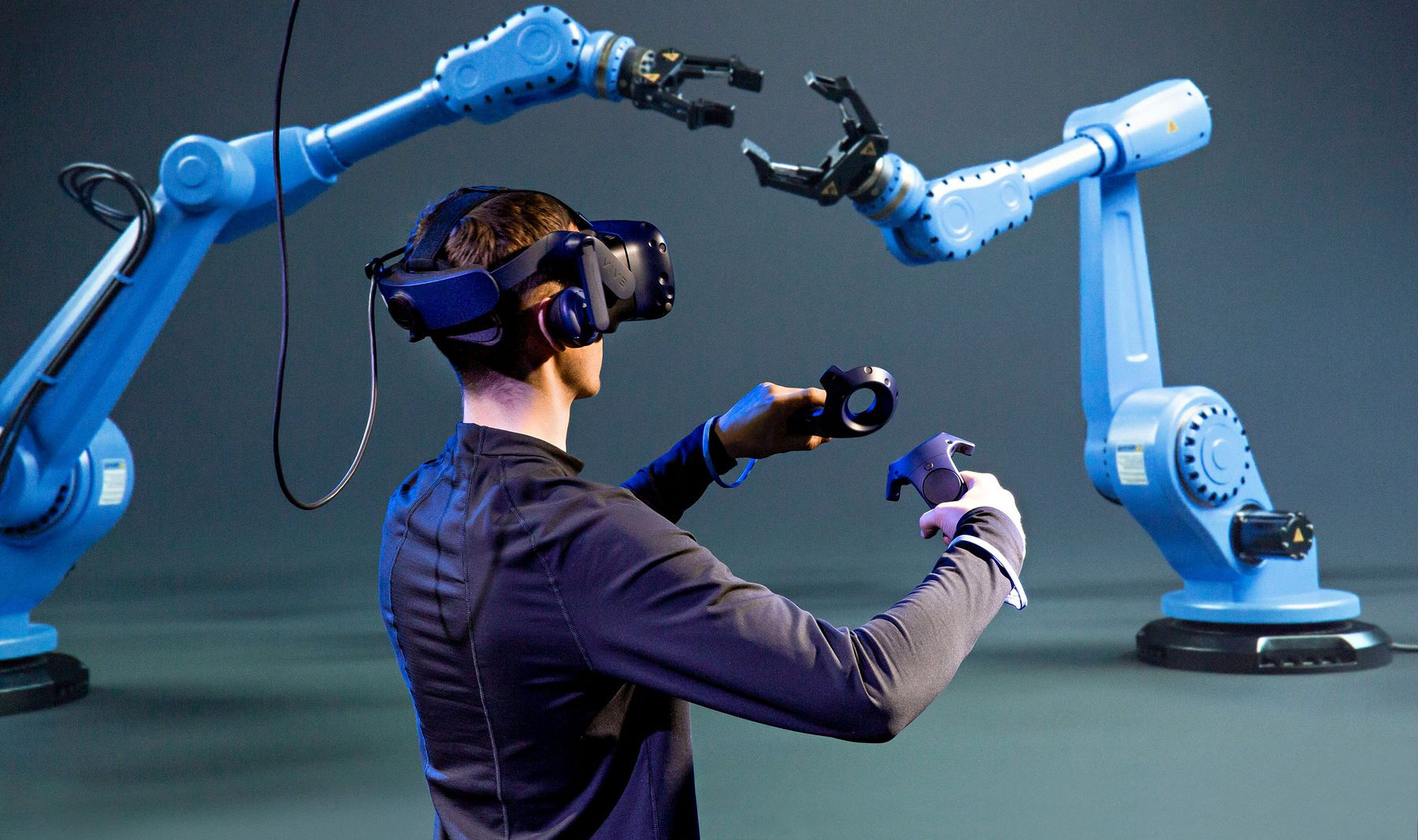 Student im Virtual-Reality-Brille im Labor mit einem Roboter-Greifarm