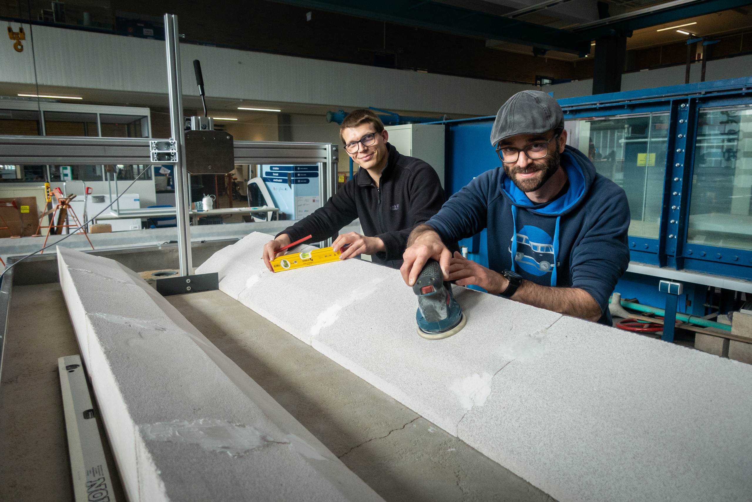 Die Doktoranden Martin Weber und Kevin Rieger über eine Betonrinne gebeugt mit Schleifwerkzeug in der Hand. 