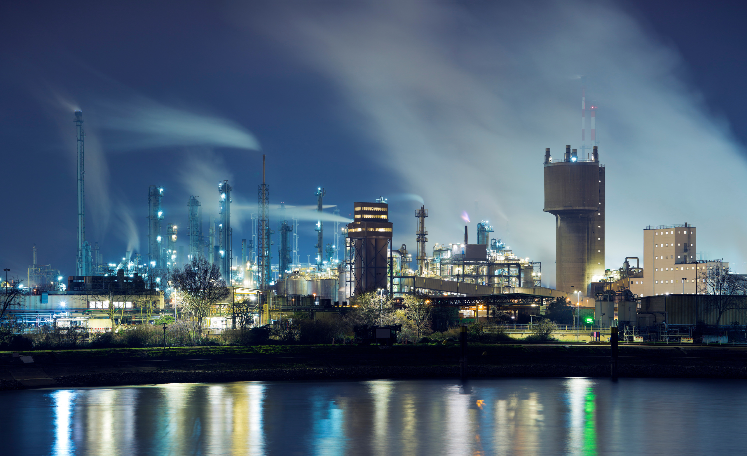 Petrochemical industry factory by a river at night Blick über einen großen Fluss auf eine Raffinerie bei Nacht