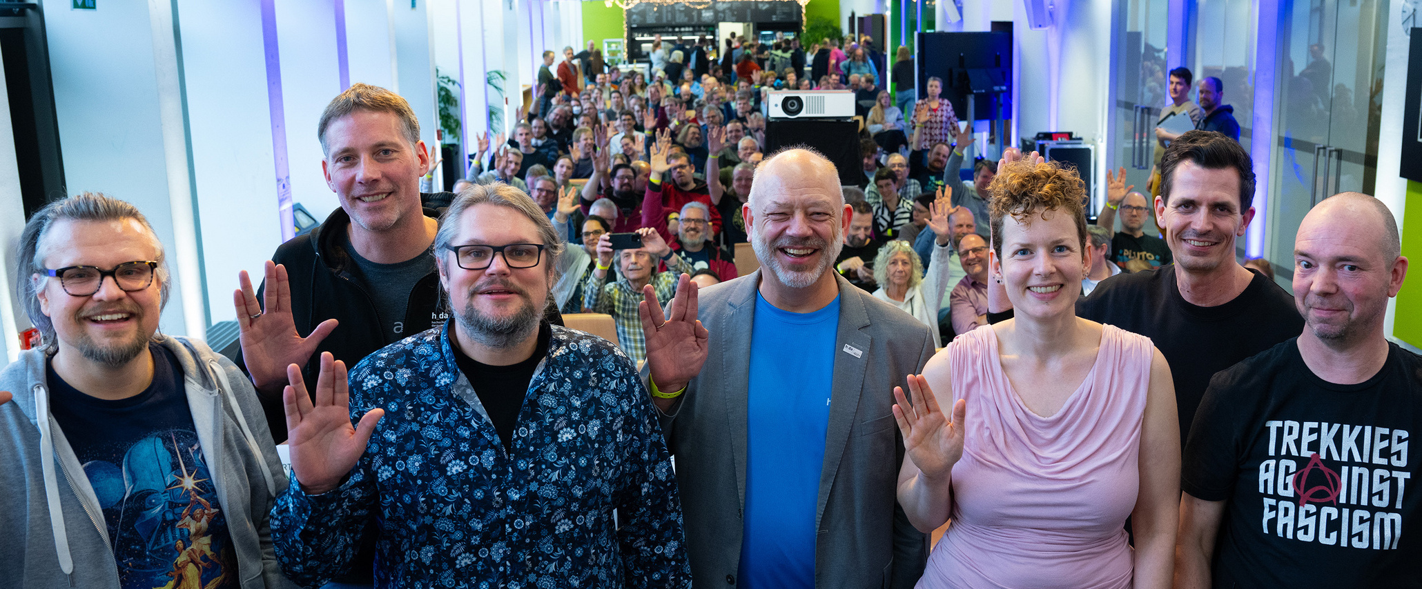 Gruppe von Panelisten im Vordergrund, Publikum im Hintergrund, alle zeigen den Vulkaniergruß