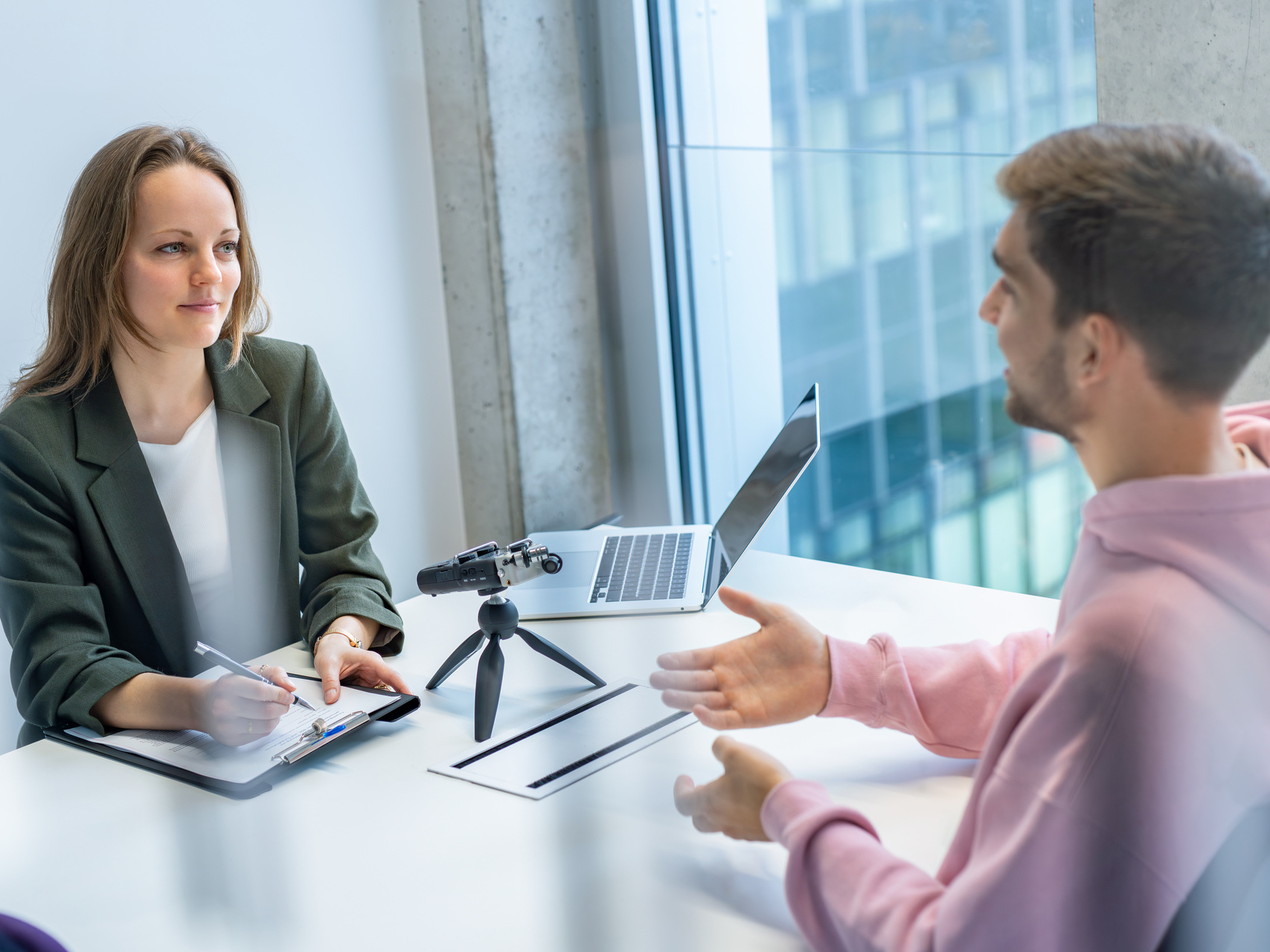 An interviewer and a test person are sitting at a table with a microphone. 