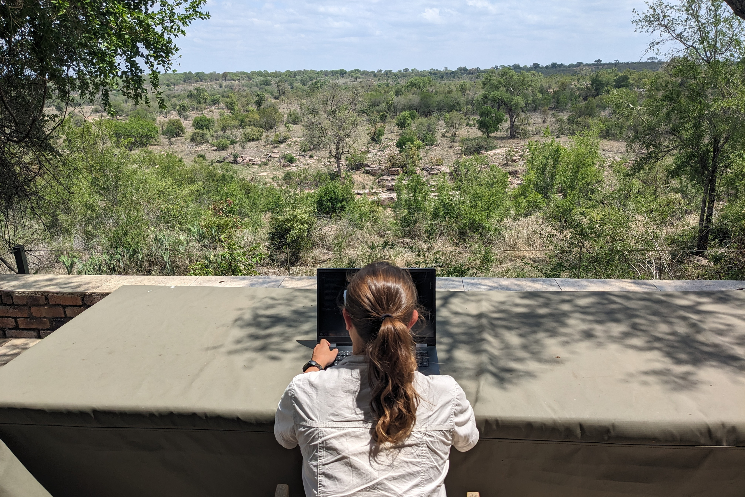 Vanessa Süßle von hinten fotografiert am Laptop arbeitend in einer Steppenlandschaft