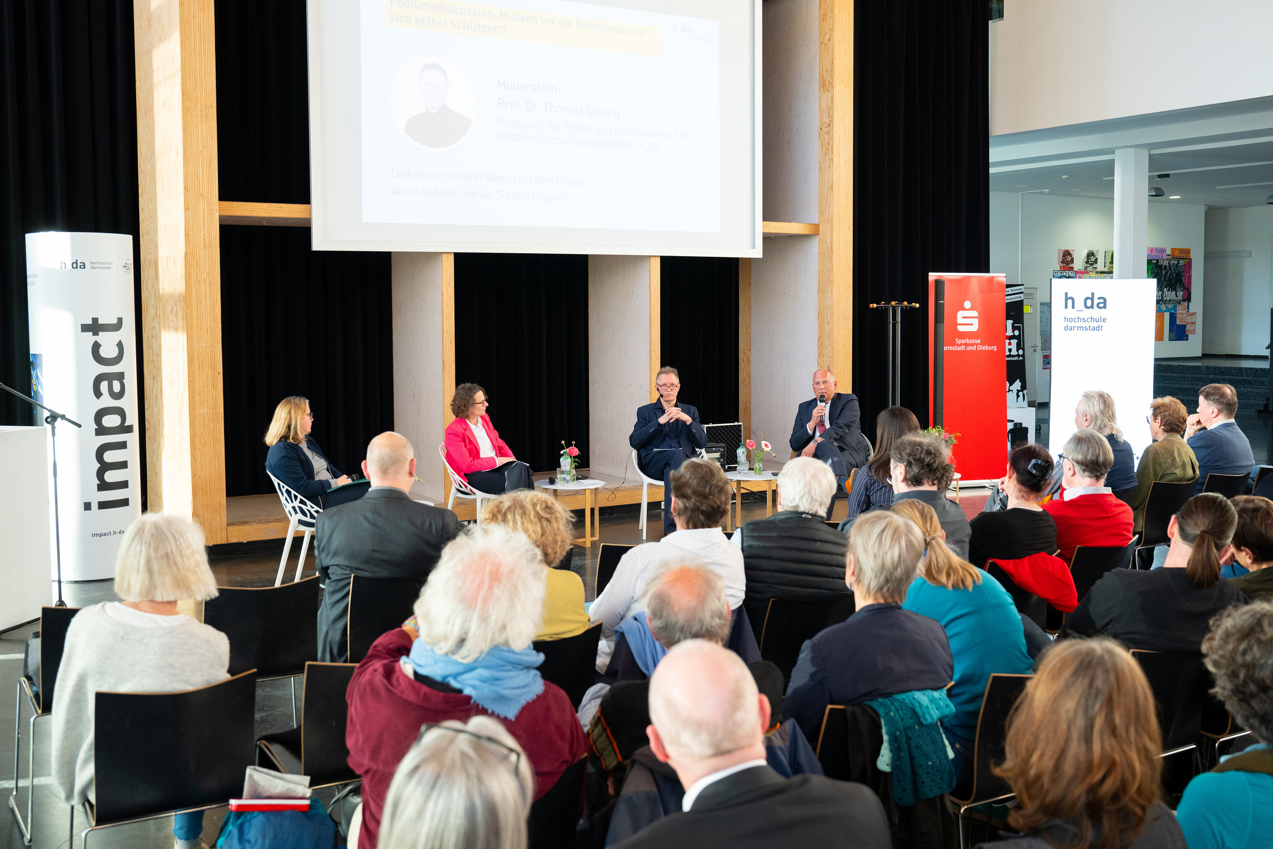 Die Vortragenden und Moderator Thomas Döring haben auf dem Podium Platz genommen.