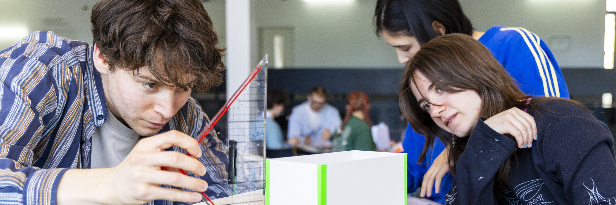 Junge Menschen an einem Arbeitstisch mit Papier, Klebeband und Linealen