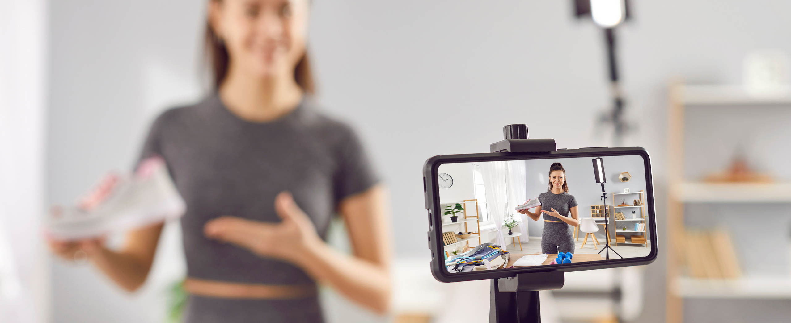 Influencerin verschwommen im Hintergrund mit Video-Handy im Vordergrund