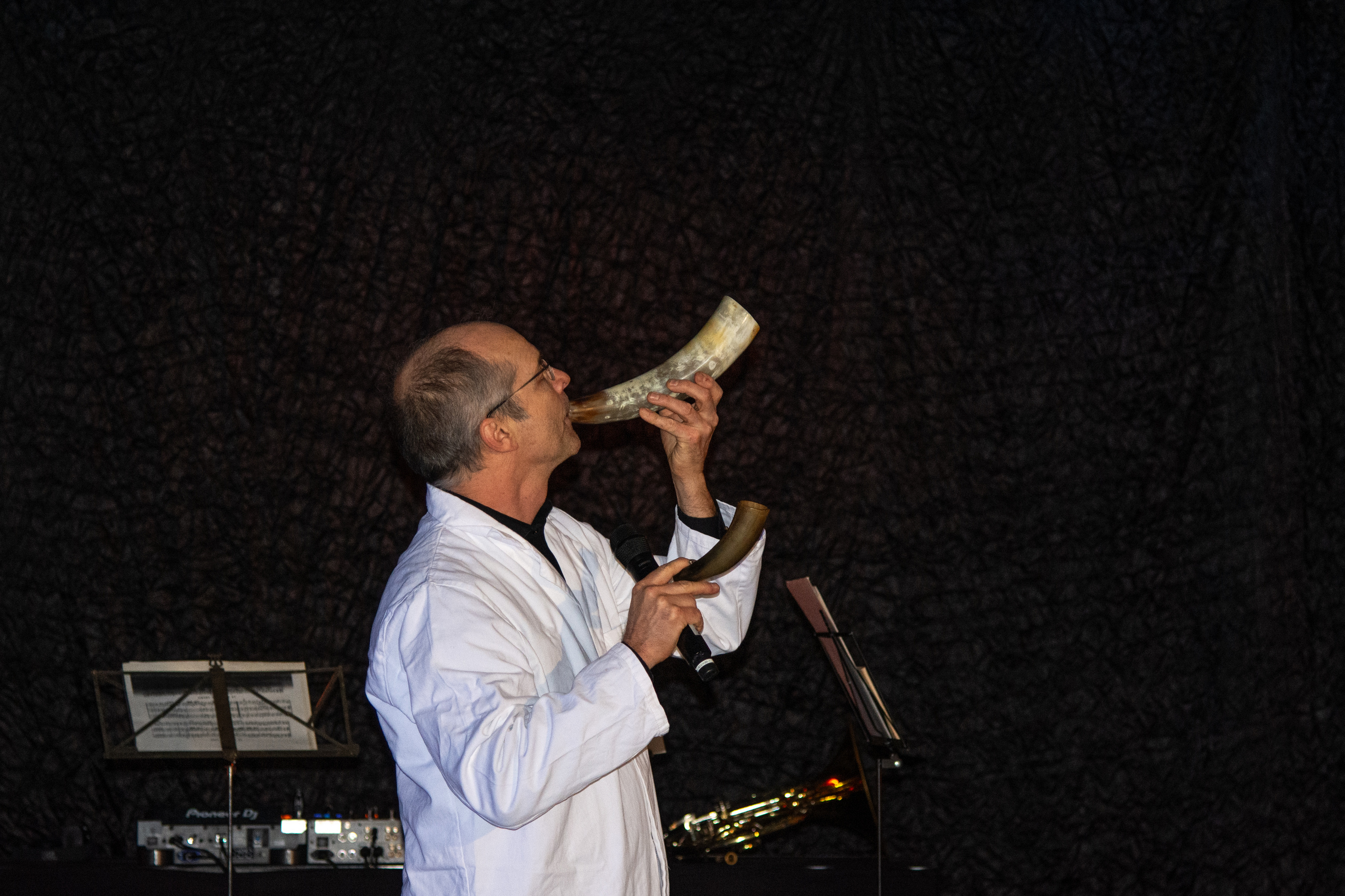 Musiker im weißen Laborkittel bläst ein Kuhhorn