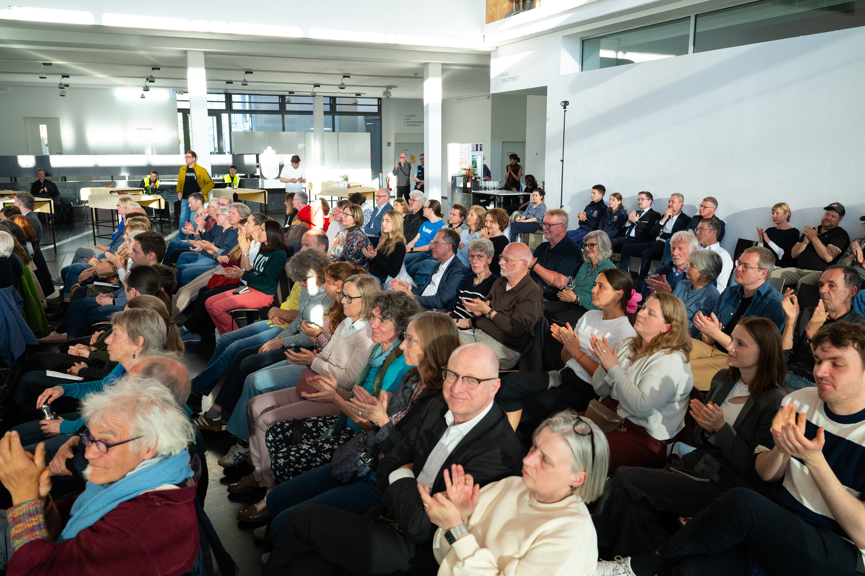 Die Gäste im Foyer applaudieren den Vortragenden.