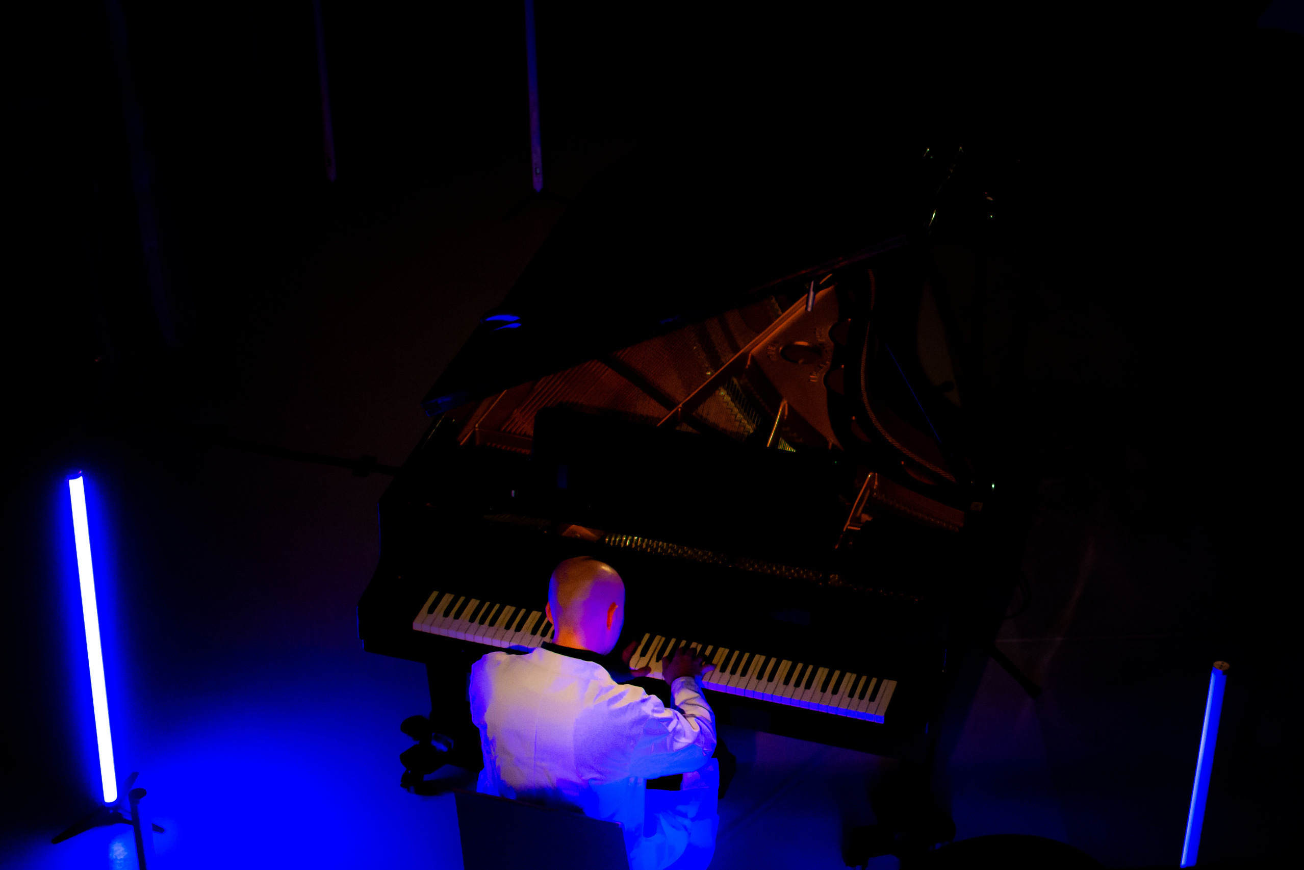 Pianist von hinten im dunklen Raum mit blauer Beleuchtung