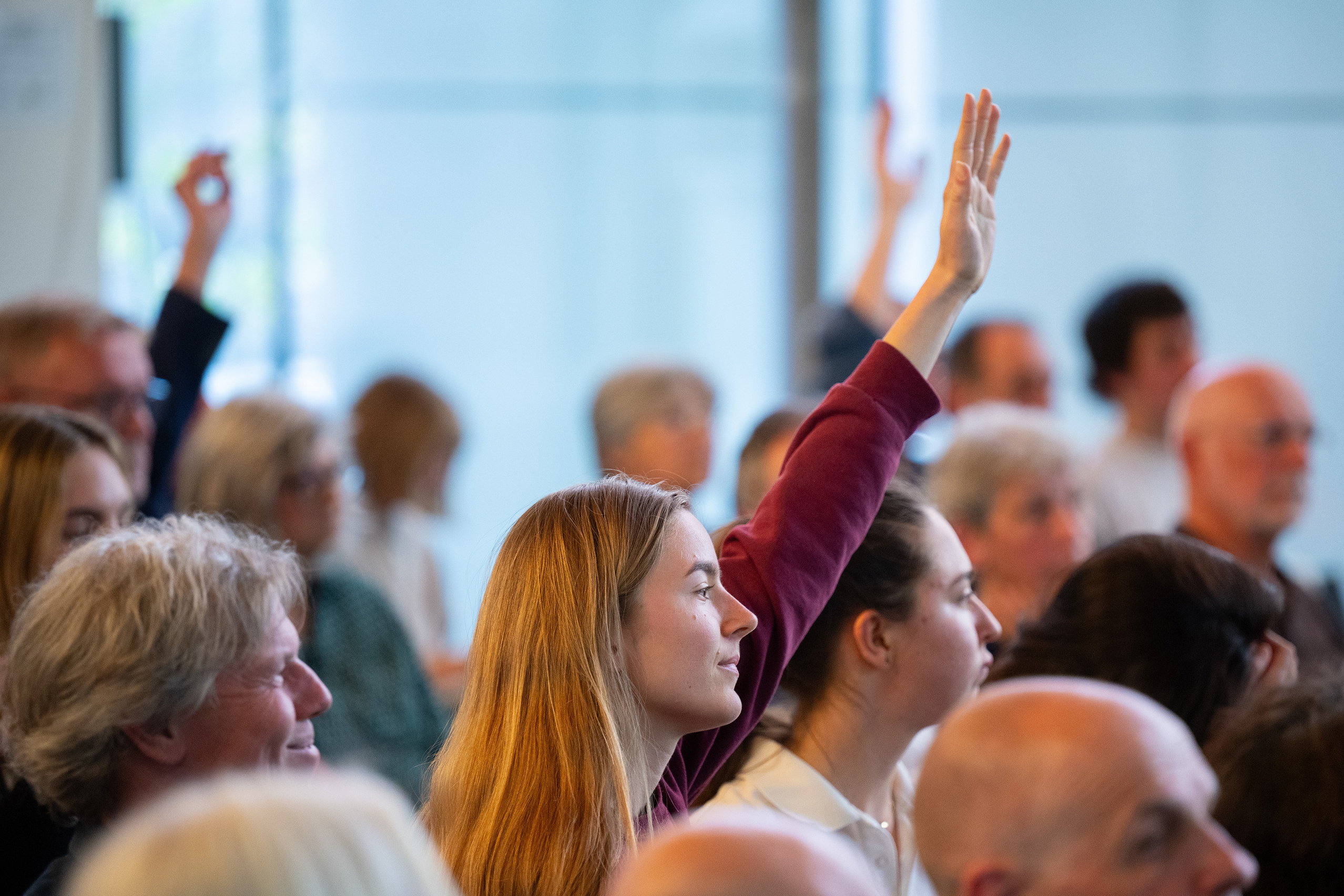 Mehrere Gäste heben den Arm, um eine Frage zu stellen. 