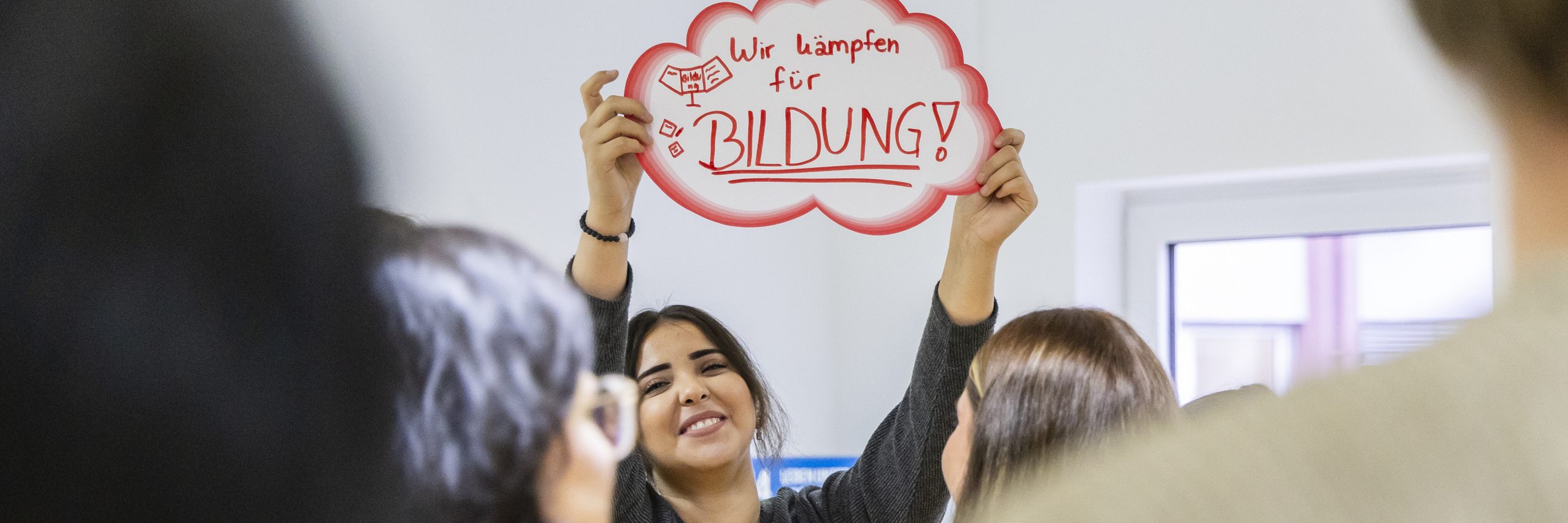Workshop-Teilnehmerin hält ein selbst gebasteltes Plakat hoch mit der Aufschrift "Wir kämpfen für Bildung"
