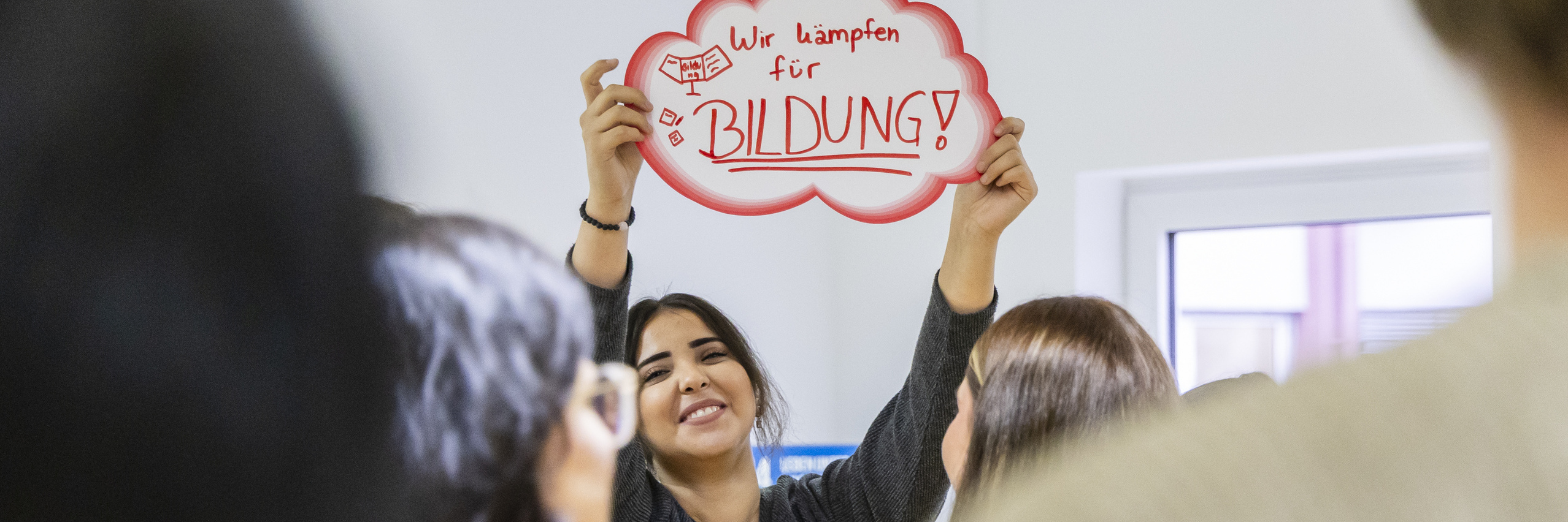 Studentin hält während des Workshops ein rot umrandetes Schuld mit den Worten „Wir kämpfen für Bildung“ hoch. 