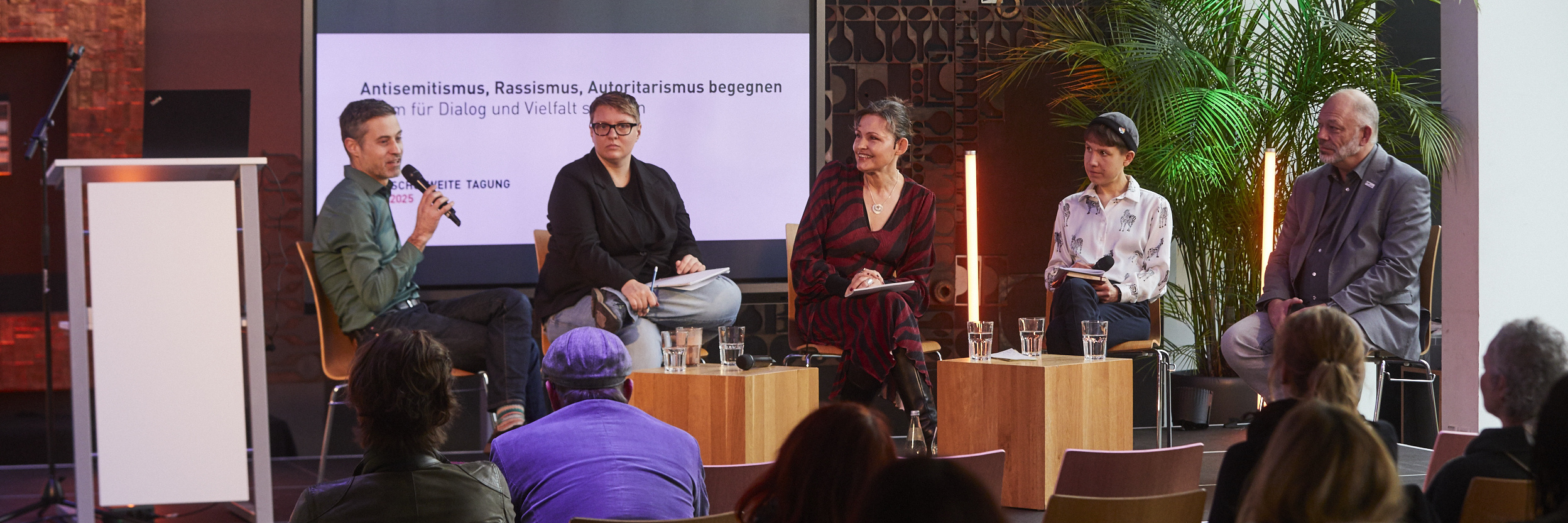 Die Referierenden sitzen auf Stühlen auf dem Podium 
