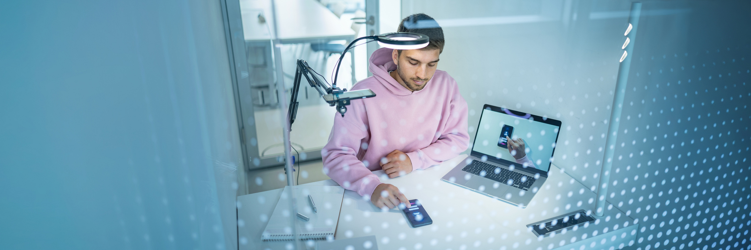 Junger Mann in rosafarbenem Pulli in einer Versuchssituation im USP-Lab mit Handy und Bildschirm