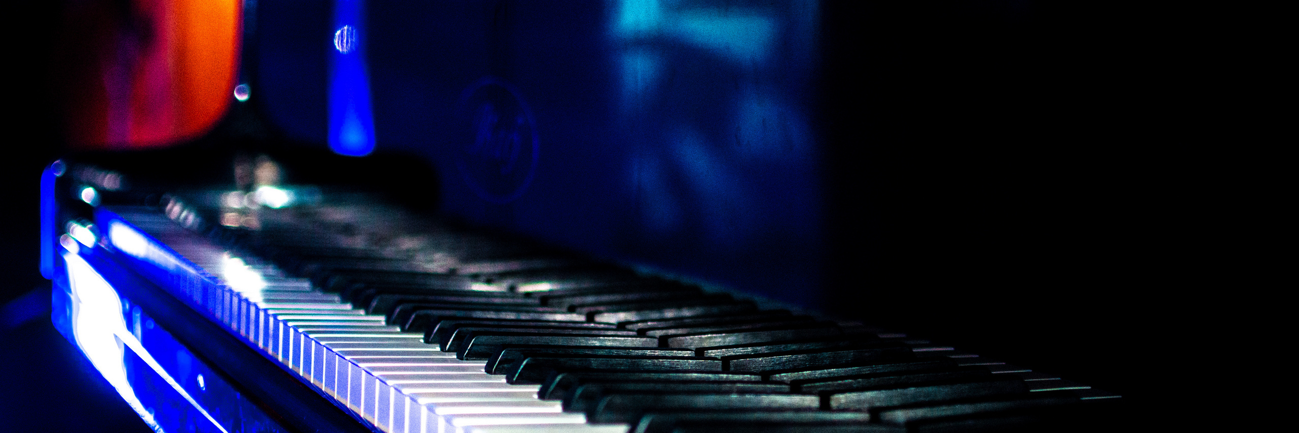 Weiße Klaviertastatur vor schwarzem Hintergrund mit bunten Lichteffekten