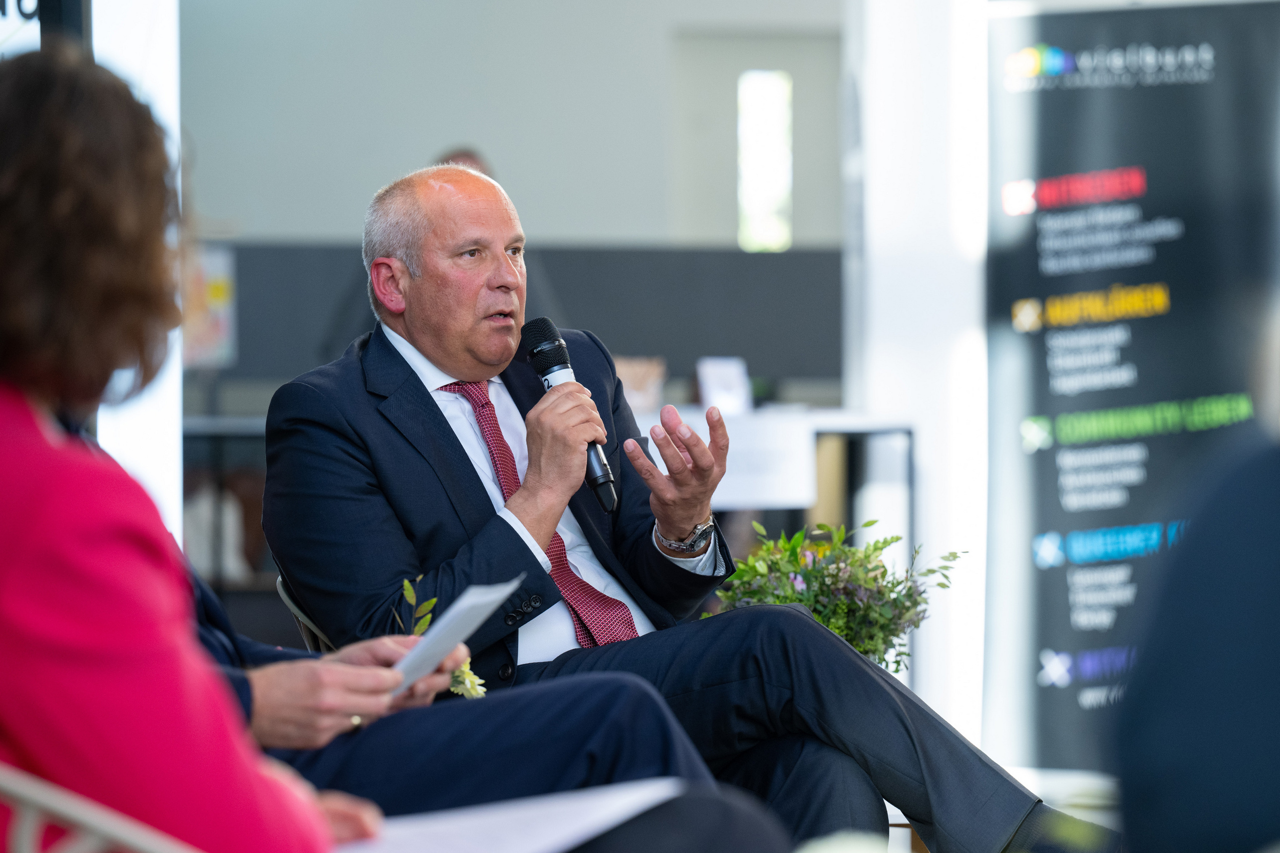 Roman Poseck sitzt am linken Ende des Podiums und spricht ins Mikrofon.