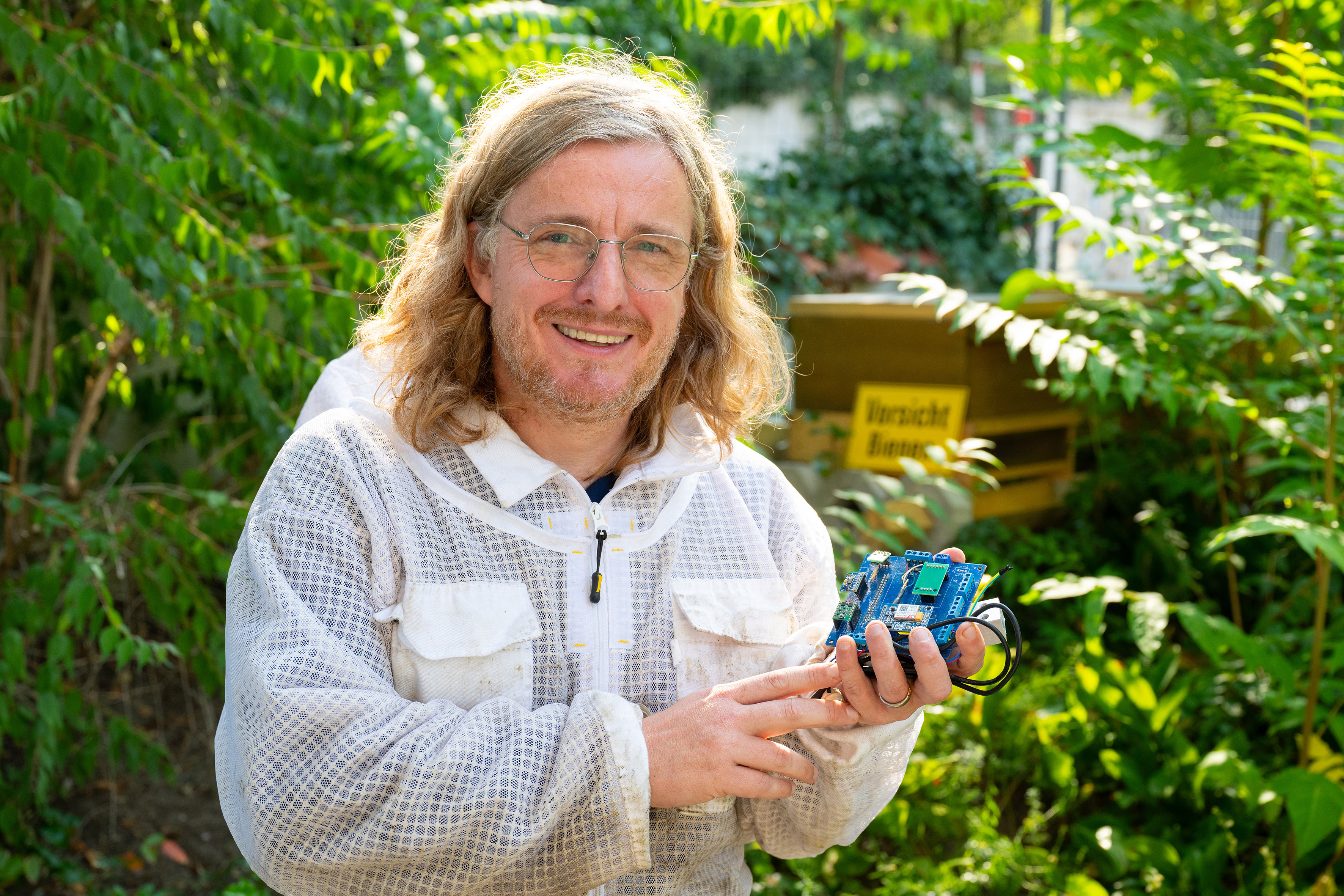 Wearing protective clothing, computer scientist and beekeeper Zinn holds a bee sensor towards the camera 