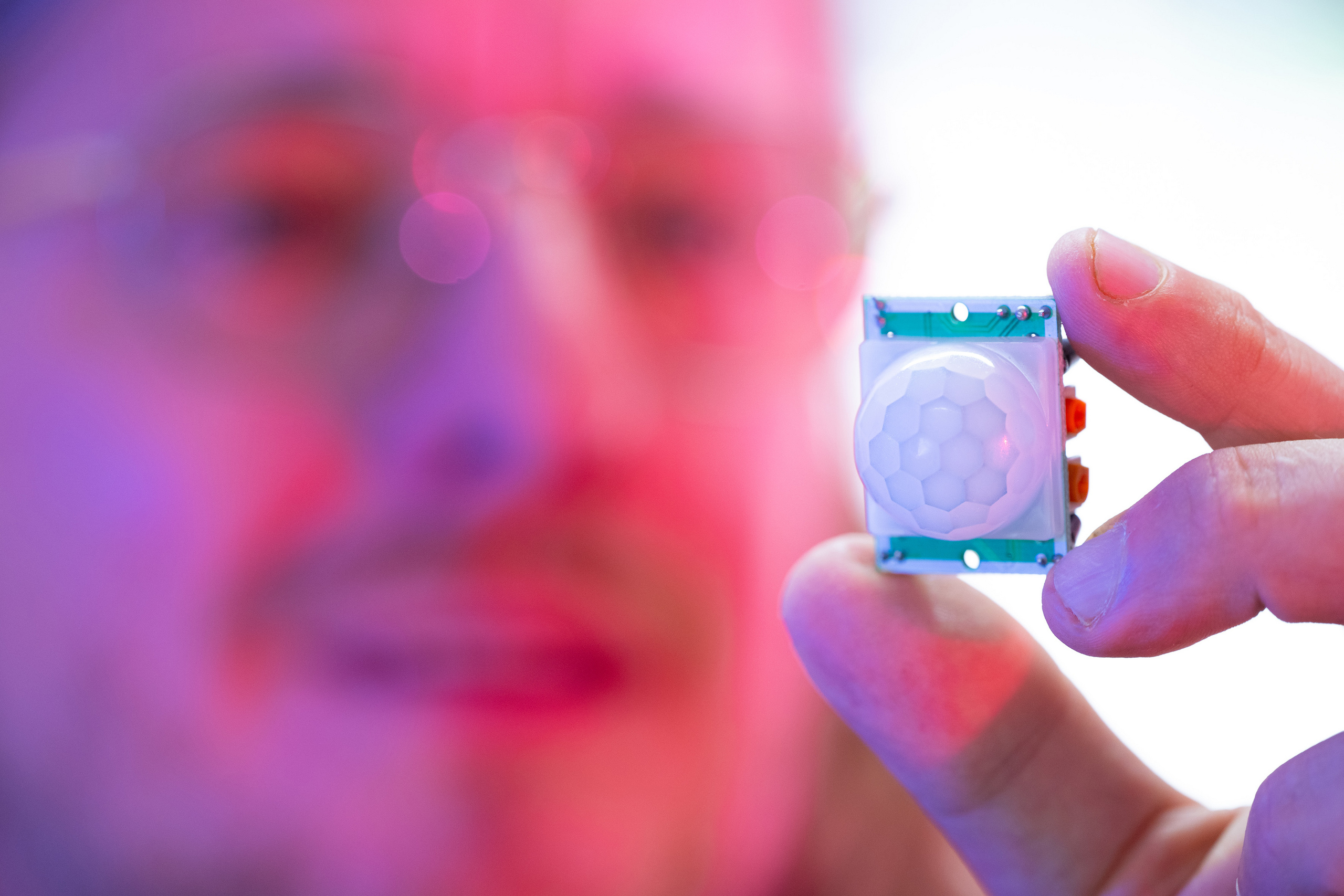 Close-up shot of Professor Zinn (blurred in the background) holding a sensor towards the camera