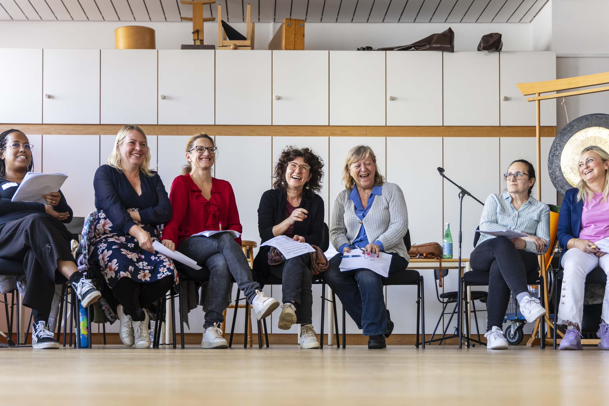 Herzlich lachende und sich offensichtlich amüsierende Chorsängerinnen sitzen im Halbkreis.