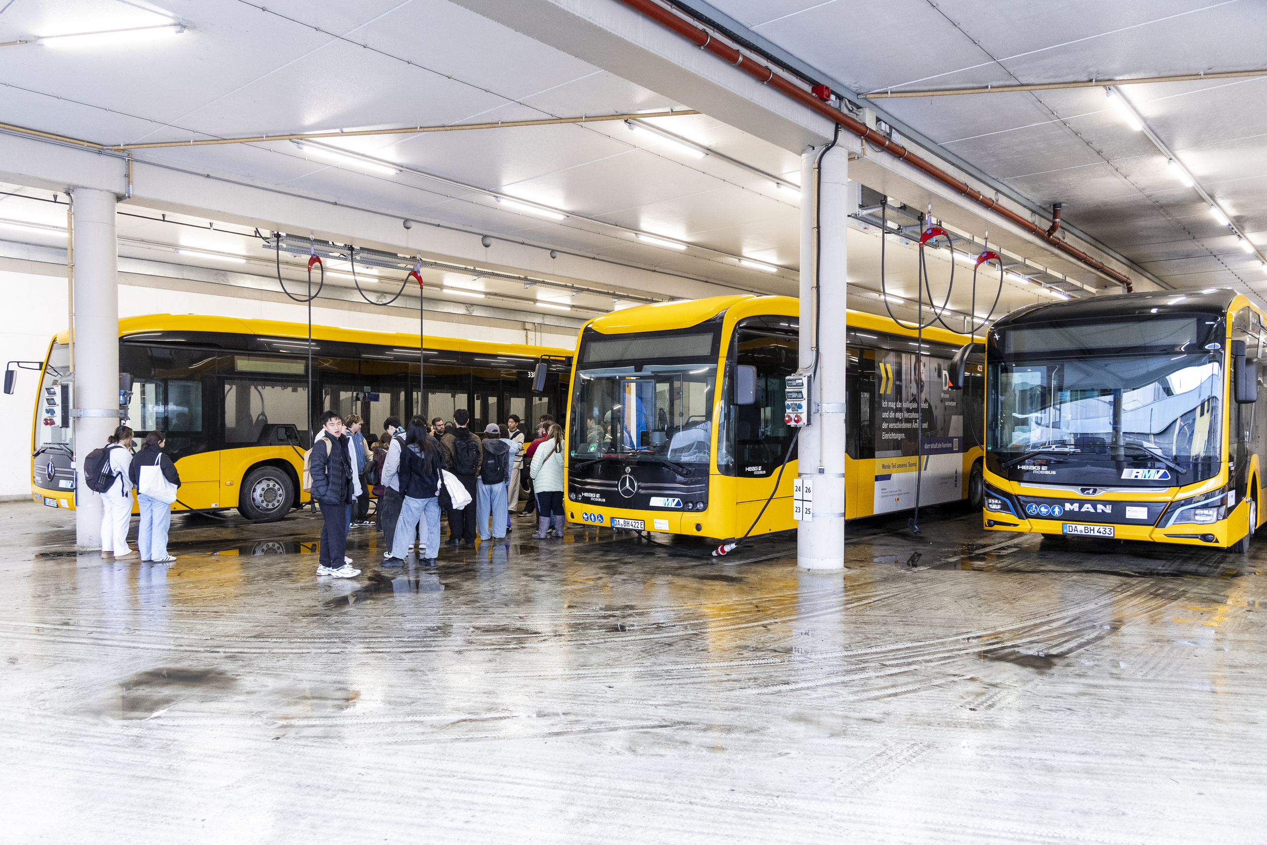 Gruppe von Studierenden zwischen den gelben Bussen im Busdepot