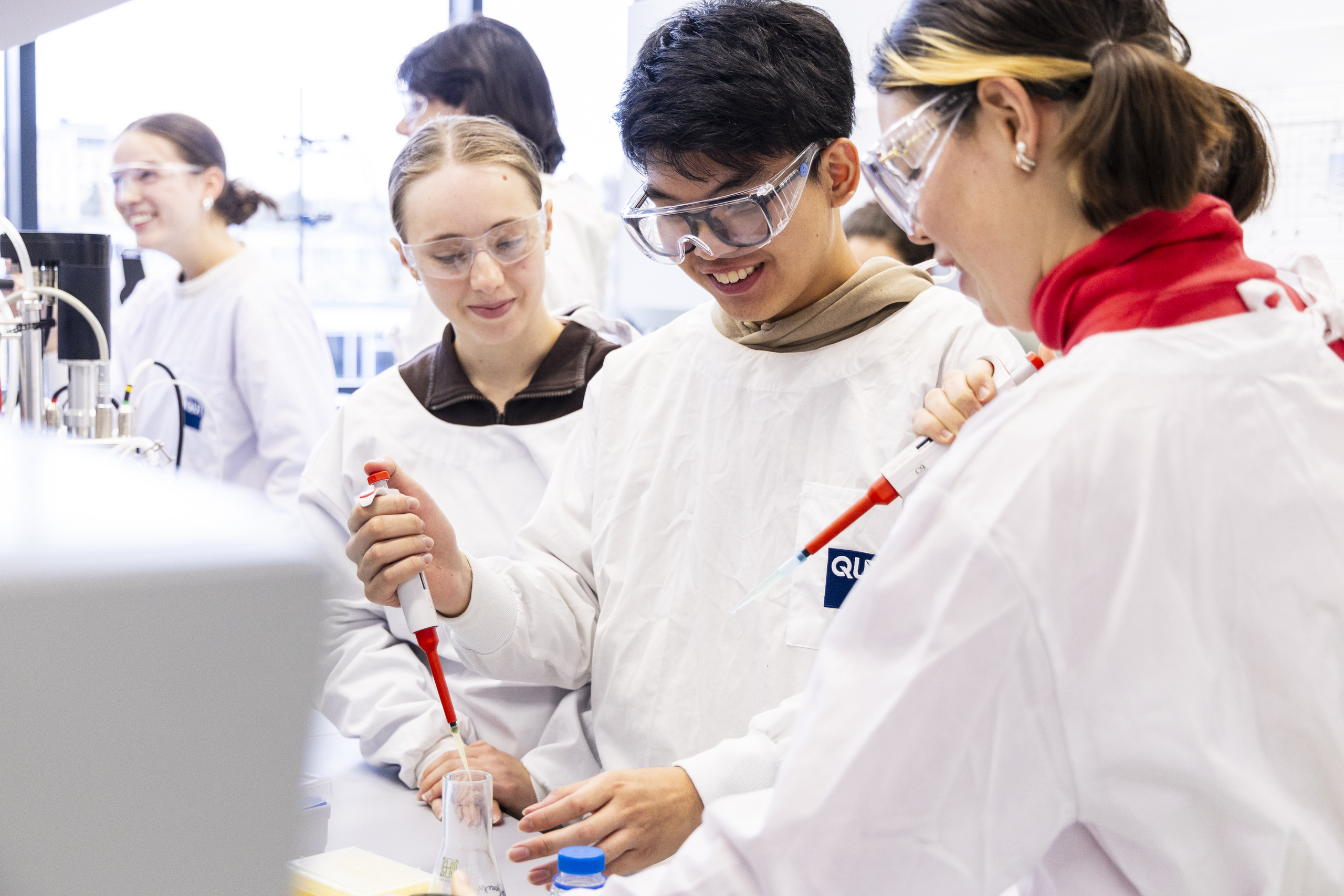 Gruppe von Studierenden in weißen Laborkitteln lächeln beim Experimentieren im Labor