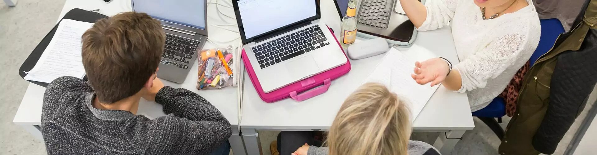 Blick von oben auf jungen Menschen in einer Arbeitssituation mit Laptops an einem Tisch