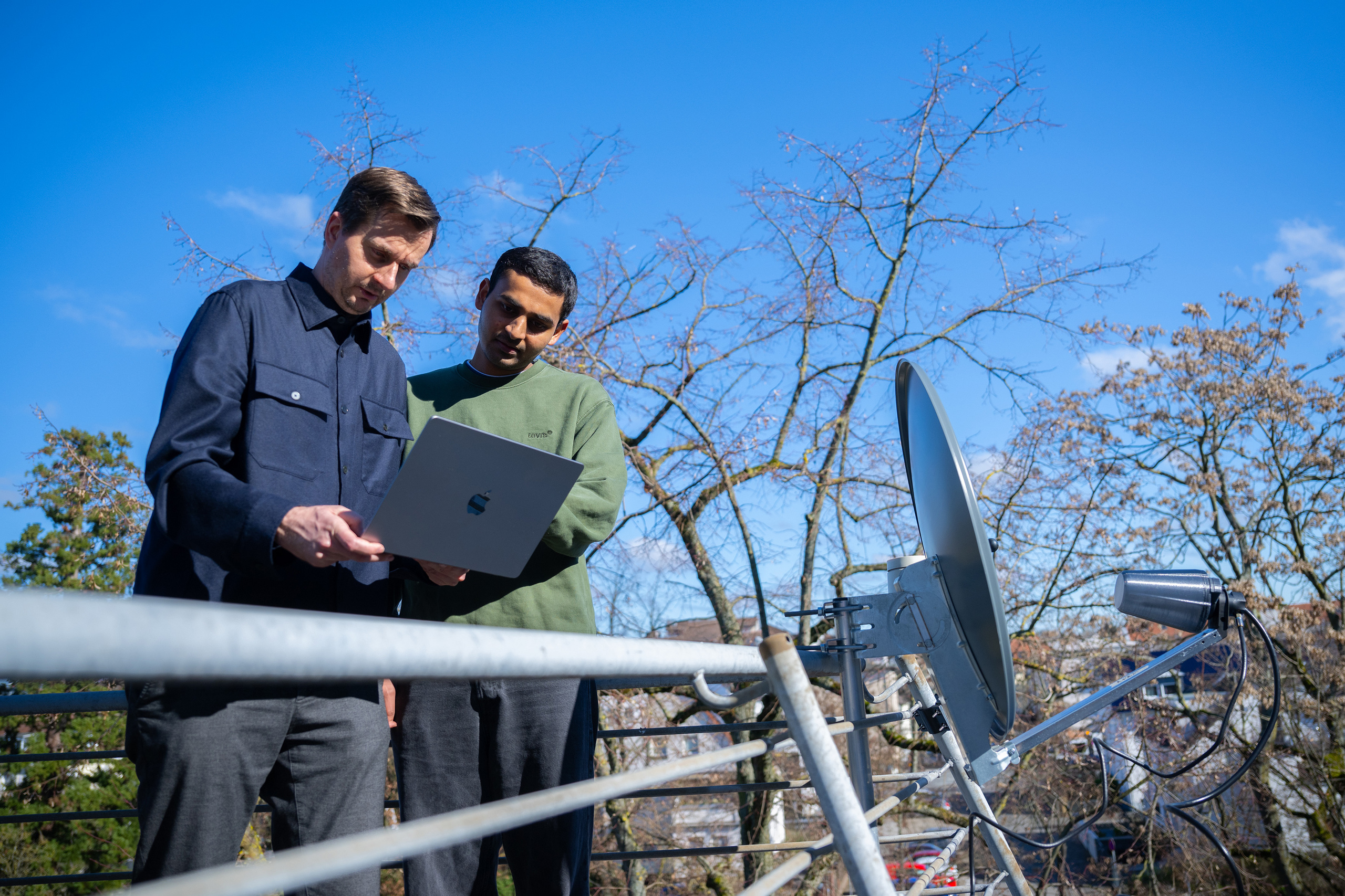 Professor Valentin und Student Vedant Vedant stehen neben der Satellitenschüssel auf einem Balkon des Fachbereichs Informatik