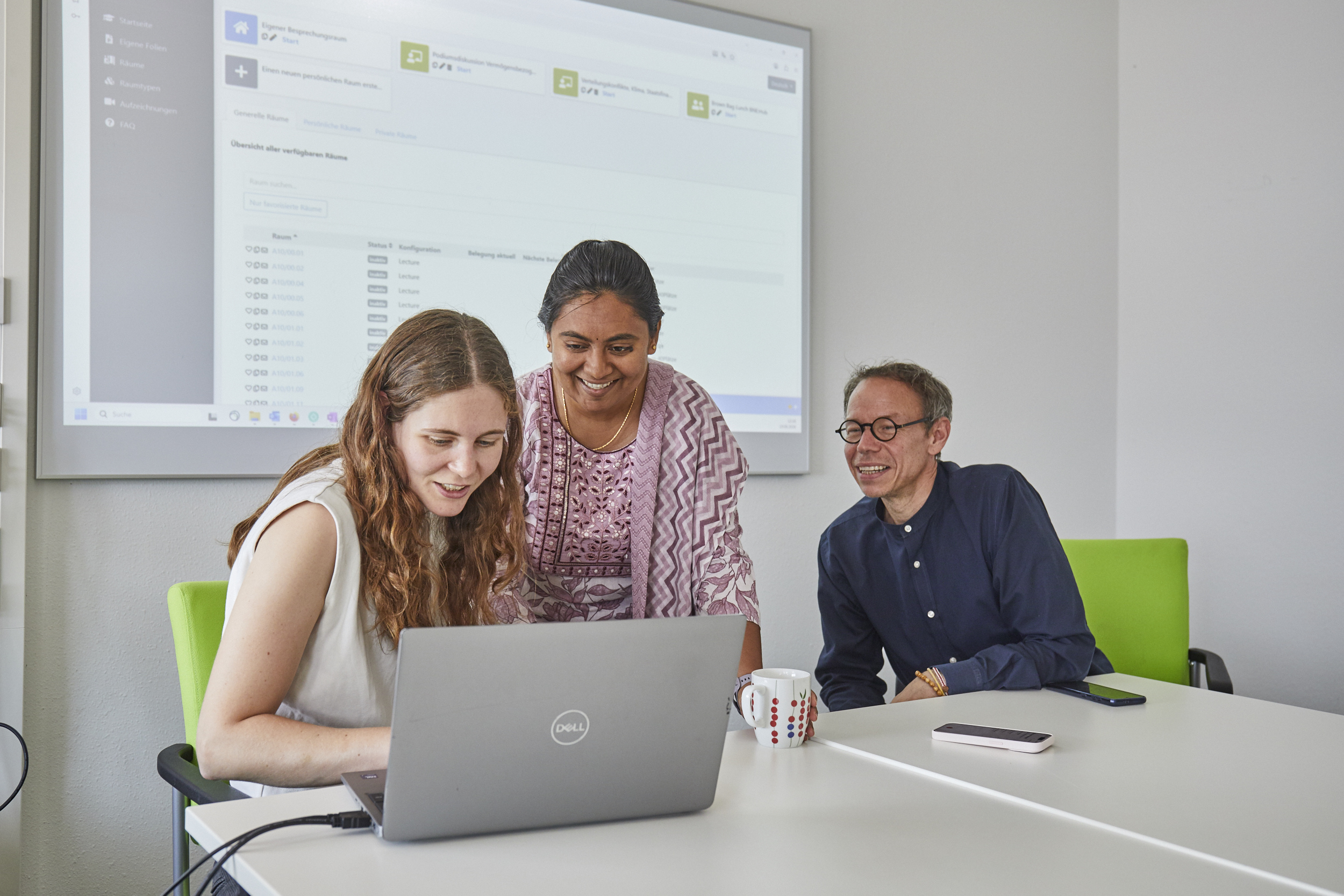 Drei Personen beugen sich über einen Laptop