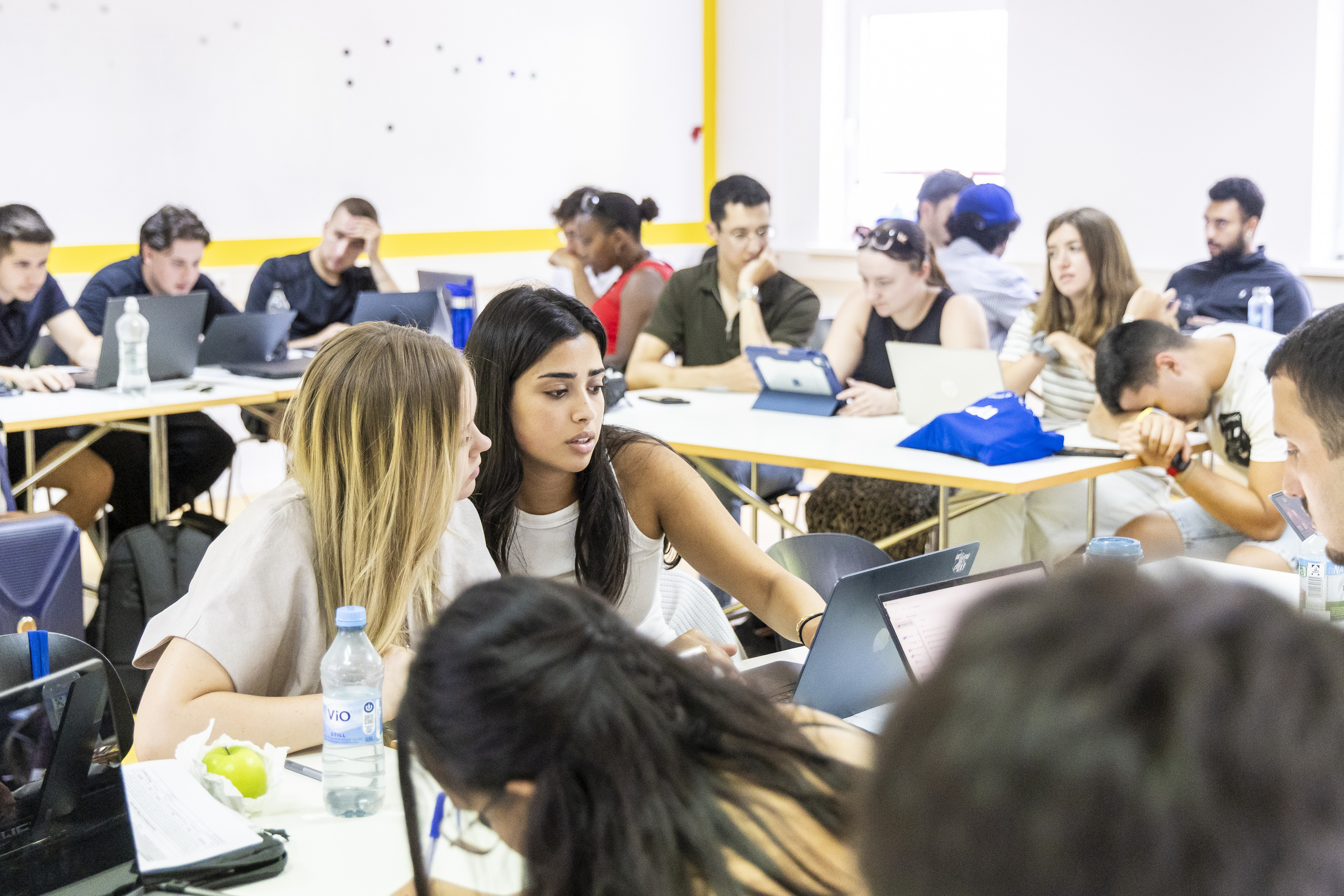   Two students discuss something on the laptop