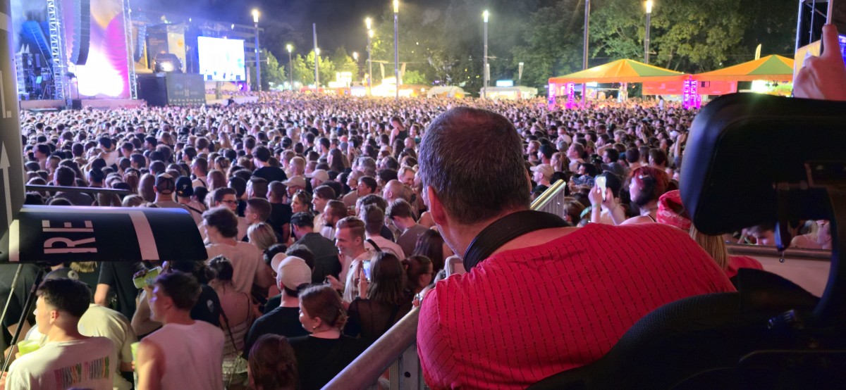 Blick über die Schulter eines Rolli-Fahrers Richtung Bühne über die Zuschauermenge beim Schlossgrabenfestival