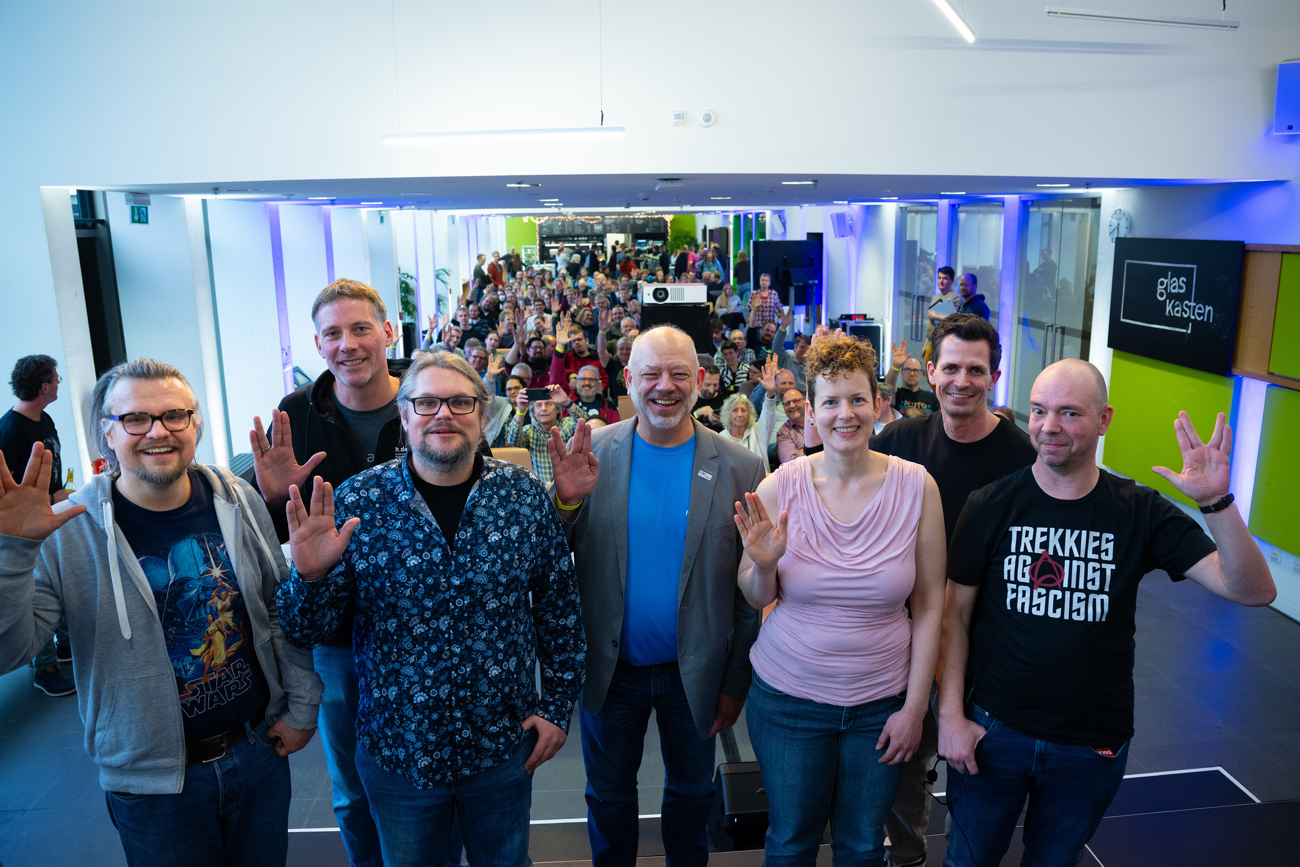 Gruppe von Panelisten im Vordergrund, Publikum im Hintergrund, alle zeigen den Vulkaniergruß