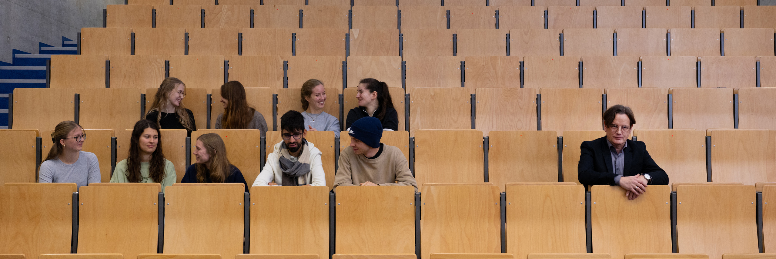 Studierende sitzen als Gruppe in einem Hörsaal, rechts davon Professor Mario Rund