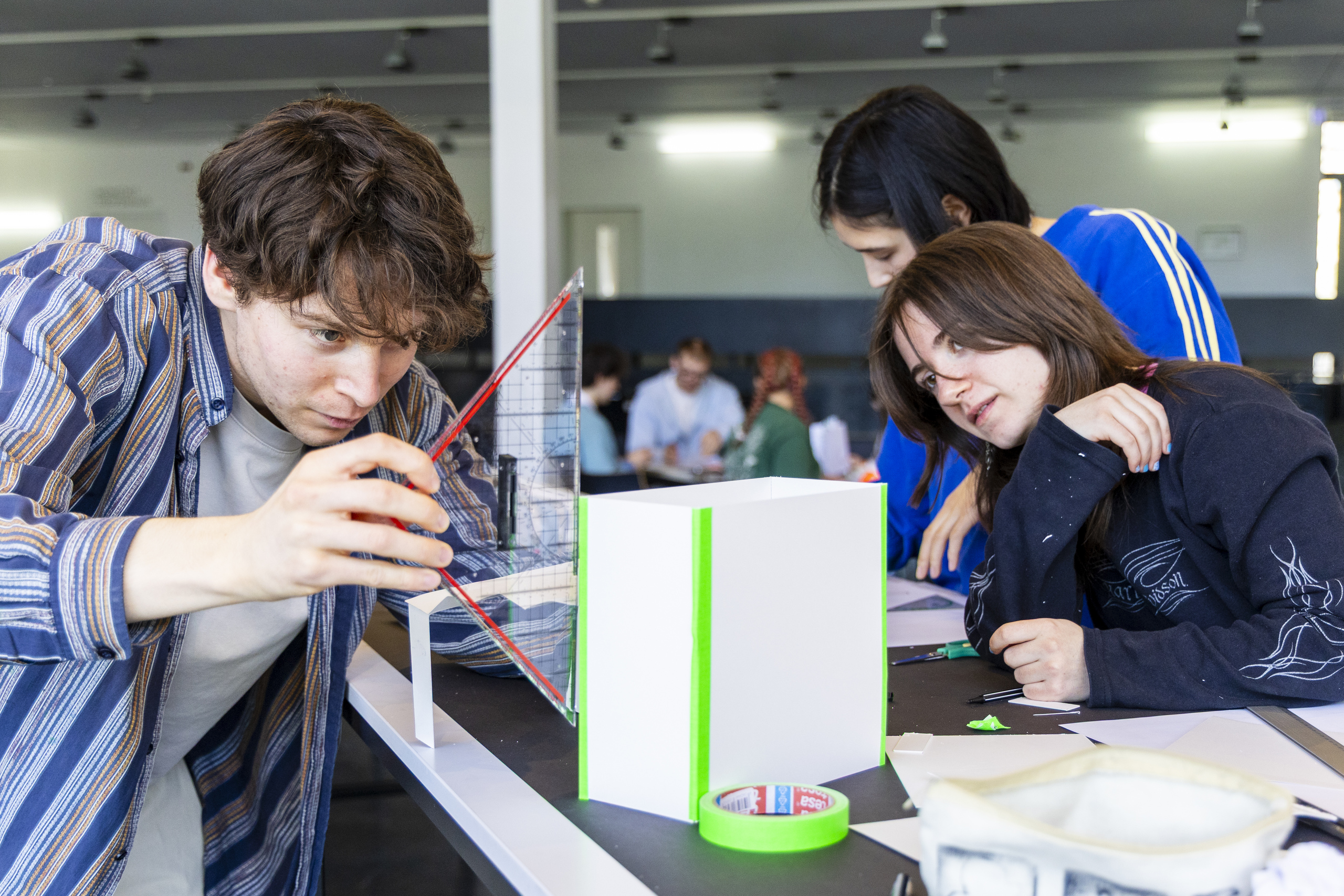Young people at a workbench with paper, tape and rulers