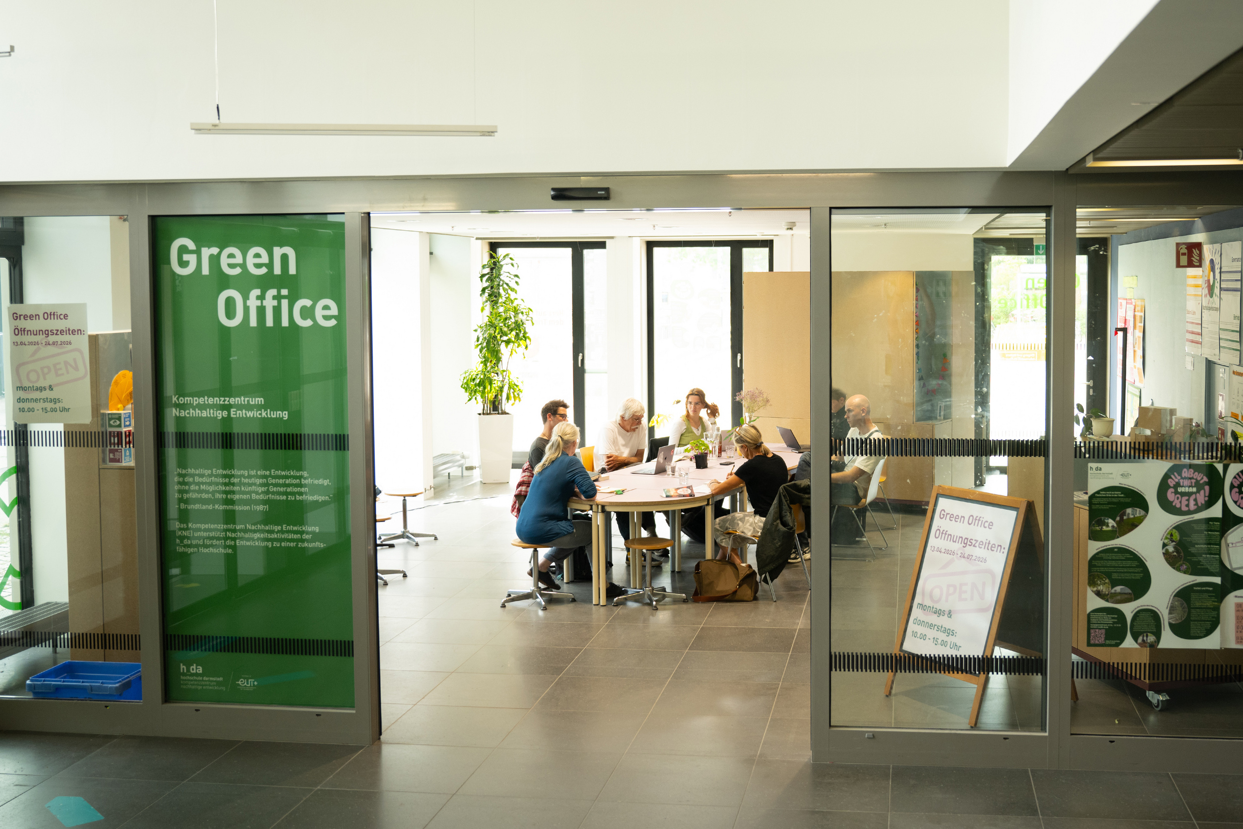 Blick in den Raum des Green Office an der h_da mit Personen an TIschen 