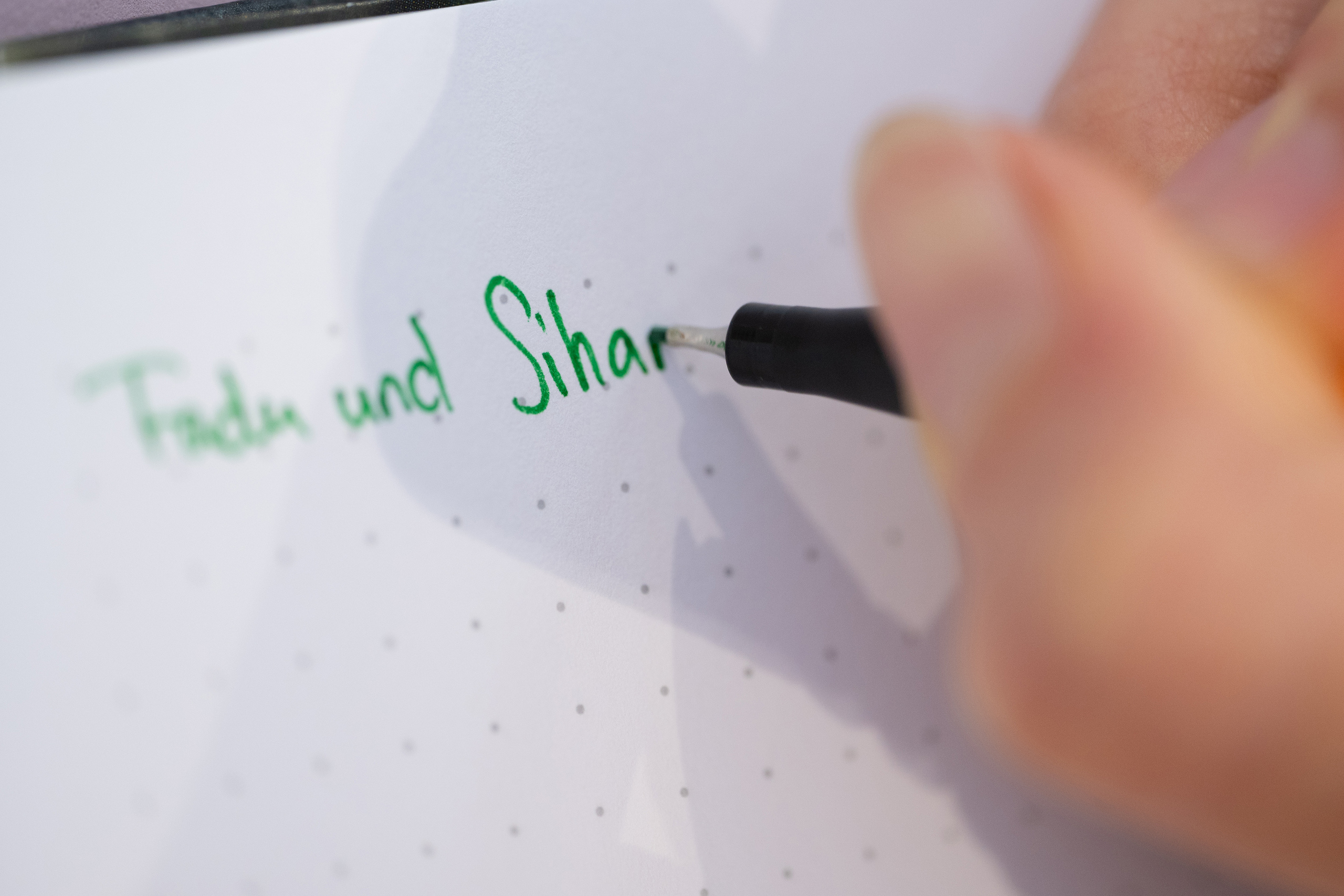 Blick auf ein Blatt Papier, eine Hand schreibt etwas darauf mit grünem Kuli