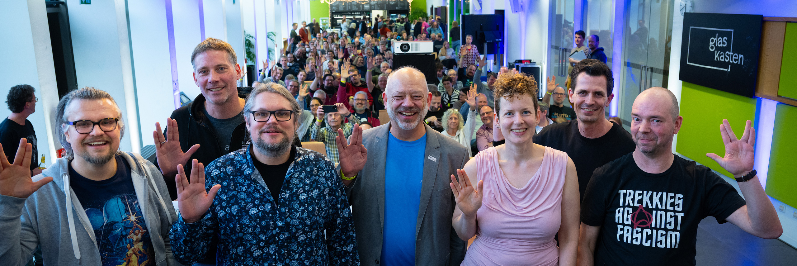 Gruppe von Panelisten im Vordergrund, Publikum im Hintergrund, alle zeigen den Vulkaniergruß